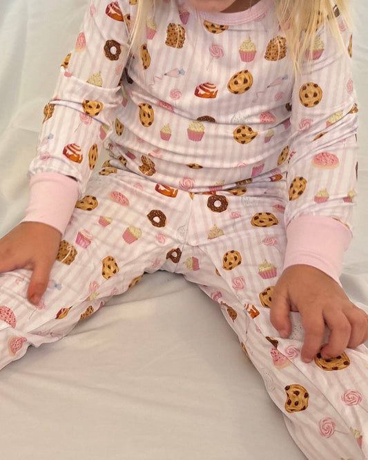 Child wearing pajamas with cookies and cupcakes pattern on a white bed.