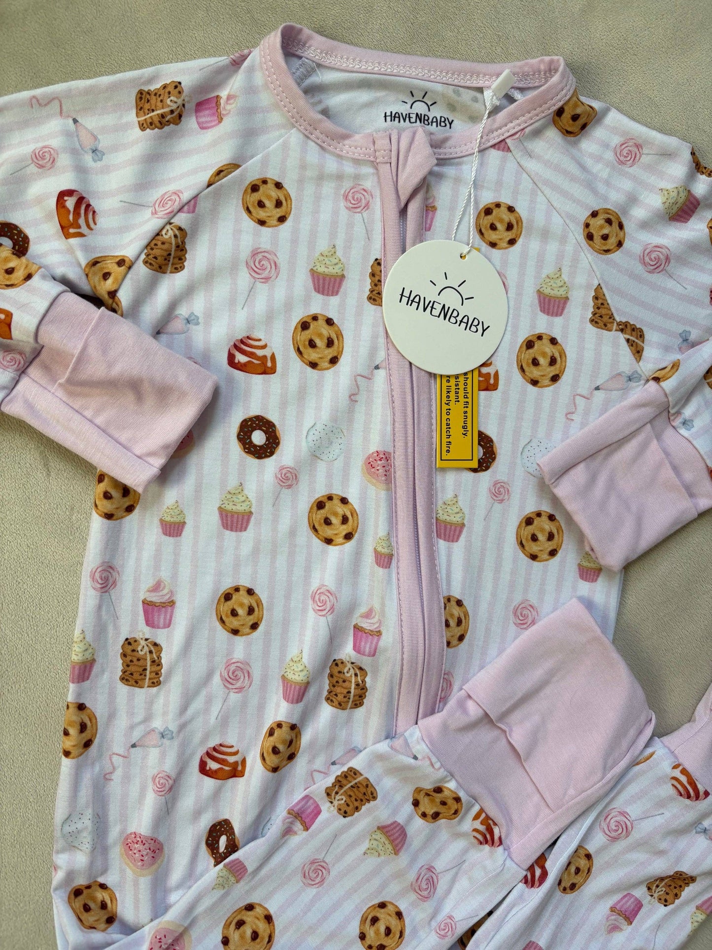 Baby onesie with cookie and cupcake pattern and pink gloves on a beige background