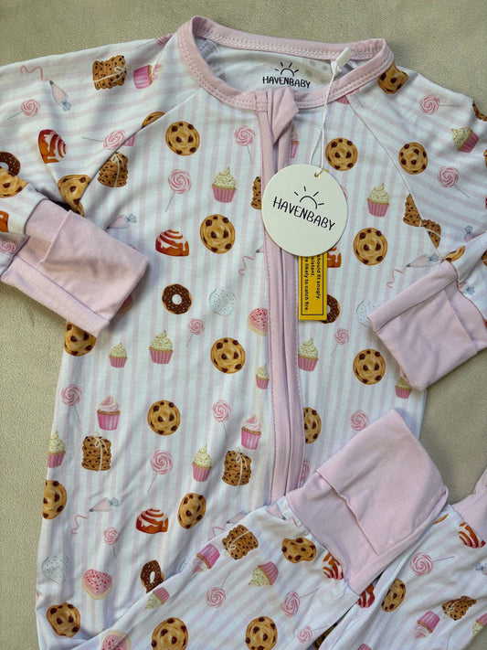 Baby onesie with cookie and cupcake pattern and pink gloves on a beige background